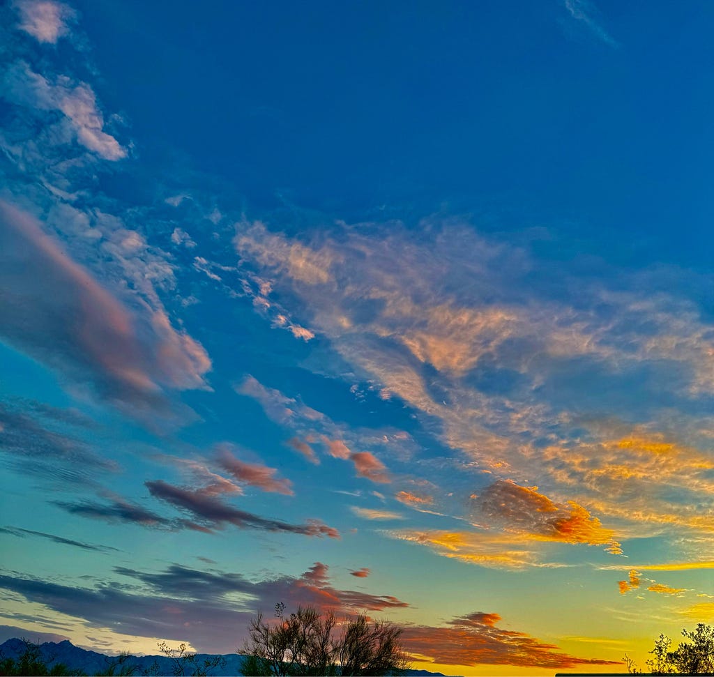 Wind swept clouds at sunrise show gold through lavender against a blue sky which becomes turquoise near the horizon.