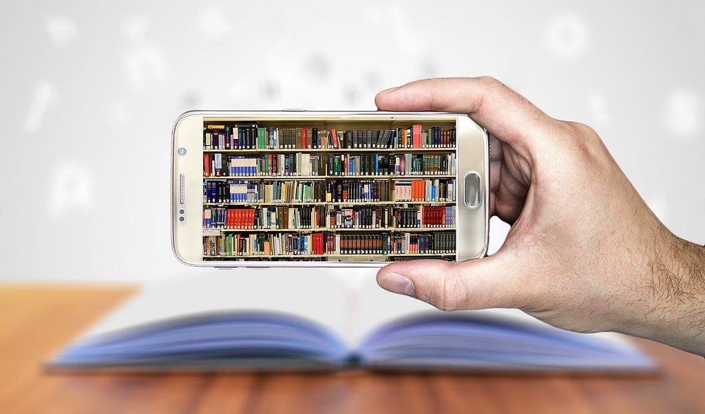 Hand holding a cell phone with shelves of books in the screen.