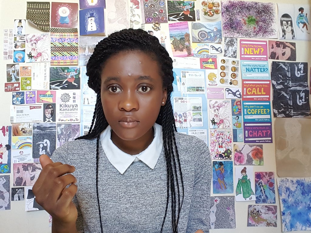A black girl sitting in front of a wall plastered with anime illustrations and memorabilia.
