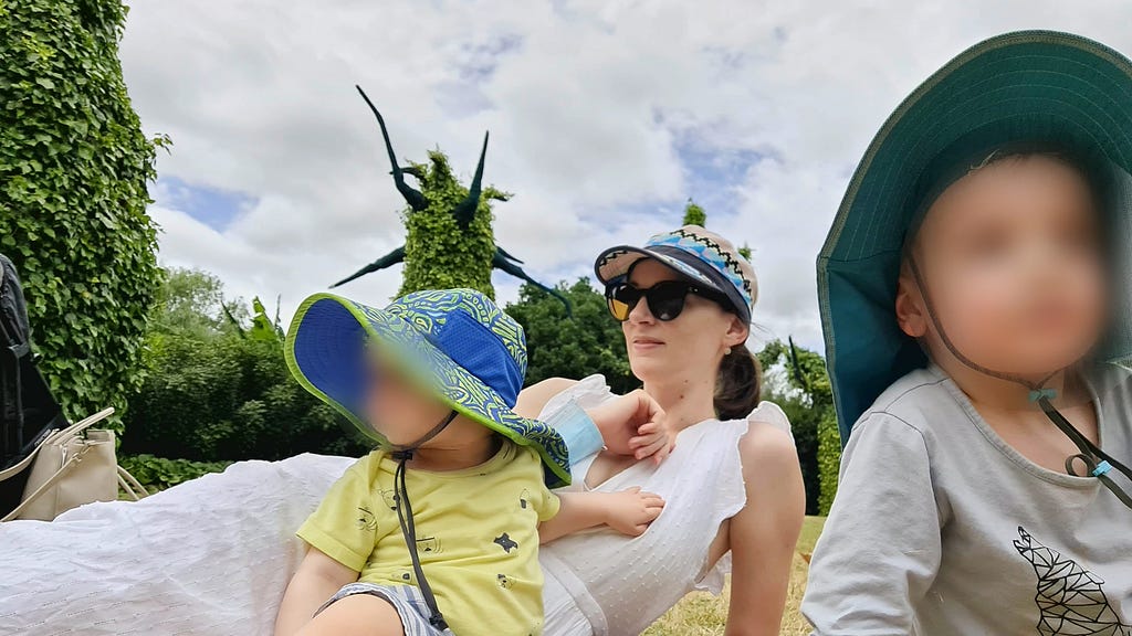 Rachael with her two sons (blurred faces) lying on the grass in Hamilton Gardens’ surrealist garden