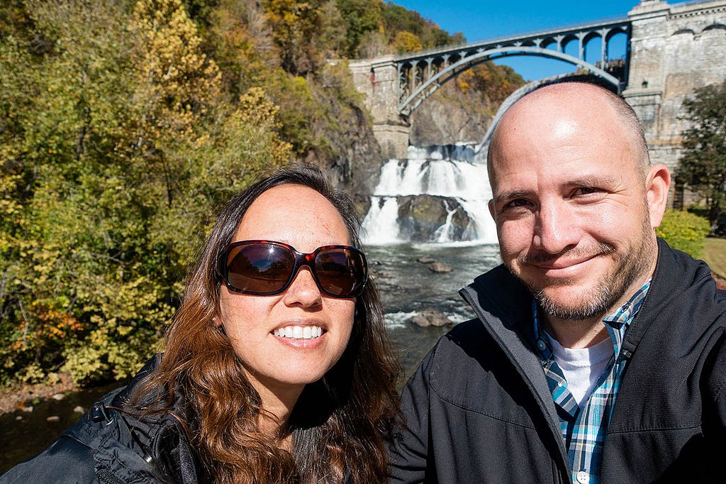 a snazzy couple in front of a bridge and waterfall