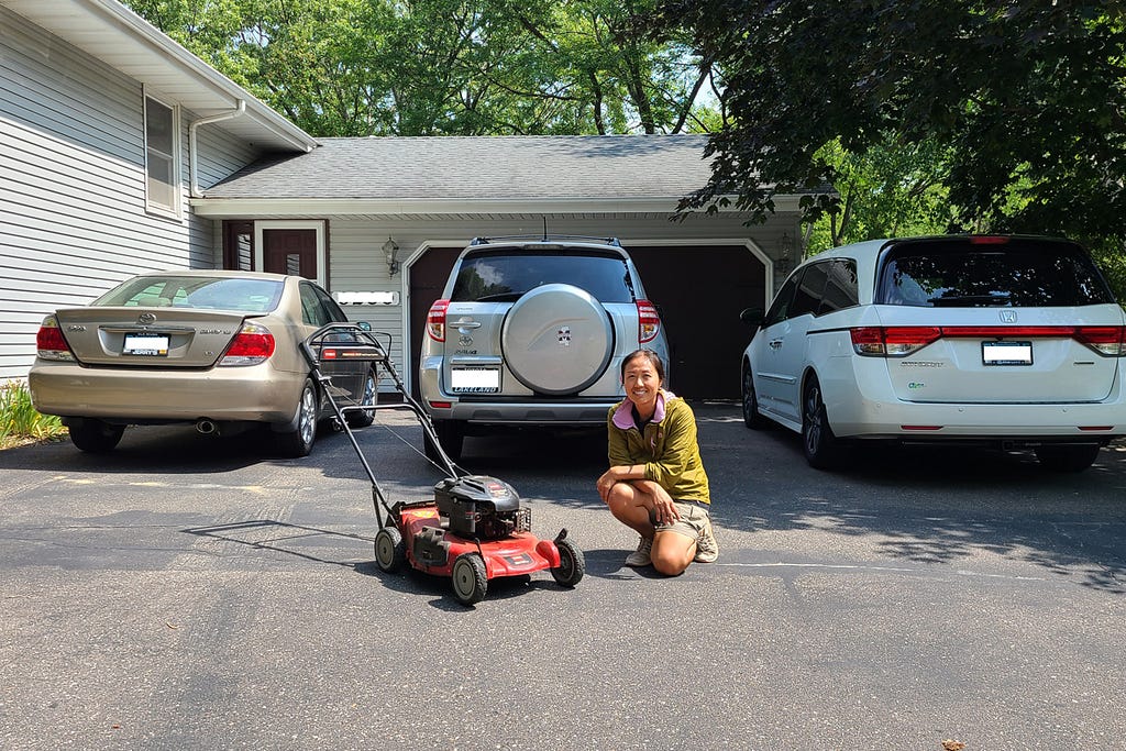 lawnup founder lady kneels infront of minivan, small suv and sedan with lawm mower