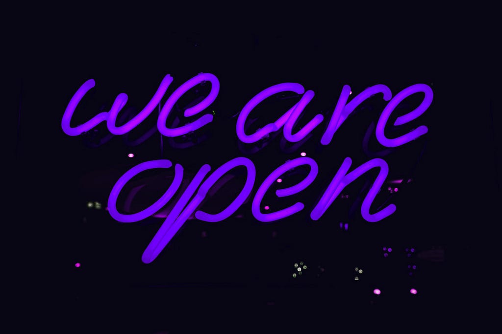 A violet neon sign, saying “we are open”.