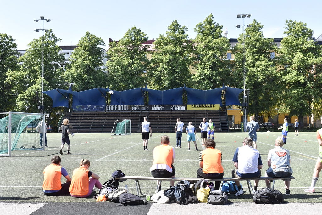 Some people playing “walking football” on a sports court while others look on from the bleachers