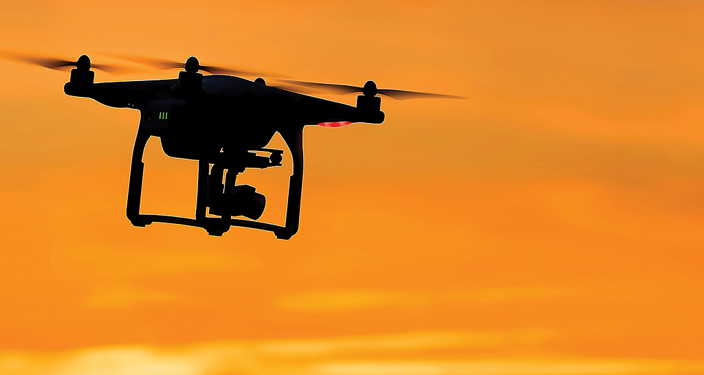 A silhouette of a drone flying in the sunset.