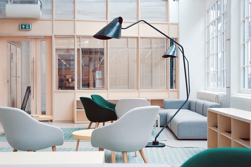 An office lounge area with blue rugs, grey and green chairs and a modern grey couch