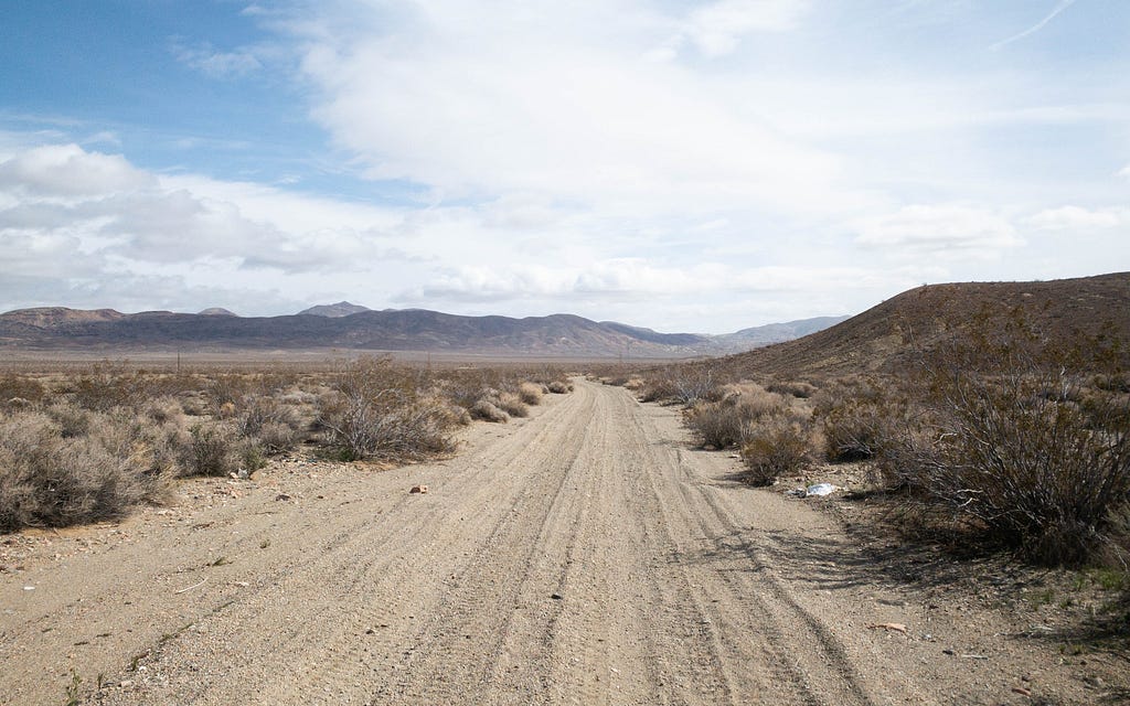 Dirt road with tire tracks in the desert. Mountains off in the distance, blue sky