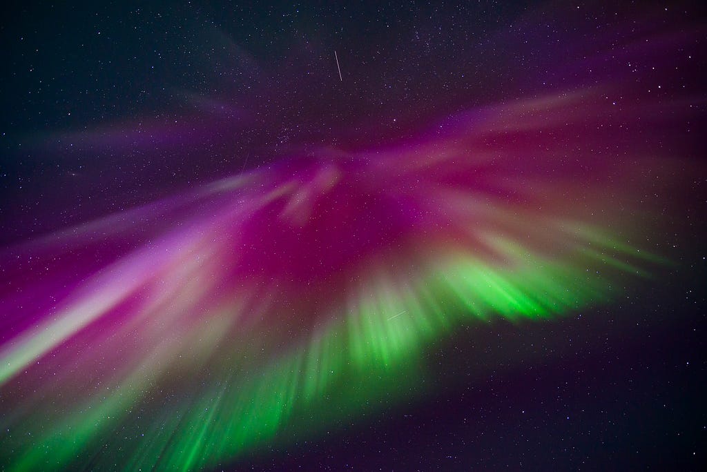 A burst of pink, red, and green light against the starry sky.