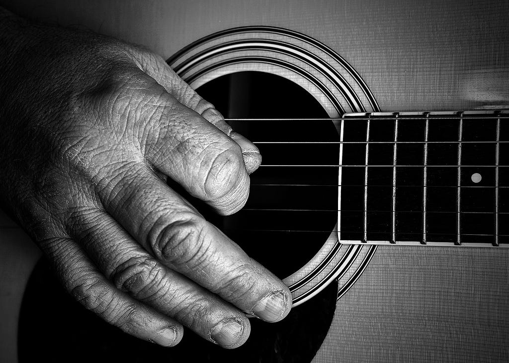 An old man’s hands playing a guitar.