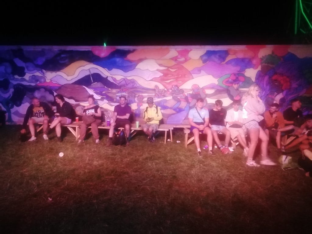 A group of people sitting on a beach with a brightly coloured abstract mural behind them.