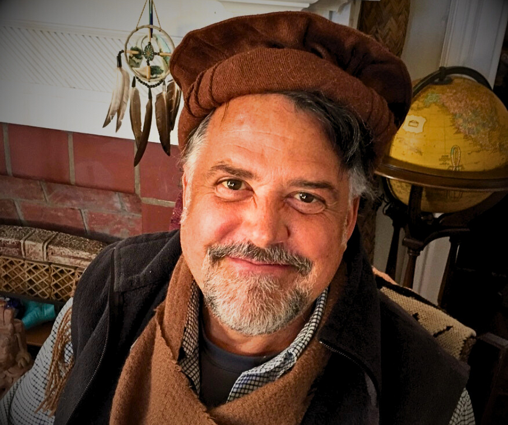 Image of H. Bruce Rinker, Ph.D smiling, in his livingroom behind him a globe and a native american dream catcher.