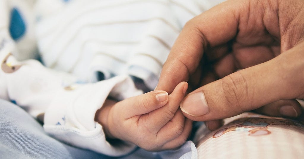 Image alt text: An image of a woman holding an infant’s hand.