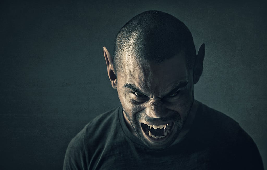 Image of a man with a fierce expression, showing his sharp fangs. He has pointed ears, adding to his menacing and otherworldly appearance. The background is dark, enhancing the intense and sinister mood of the scene.