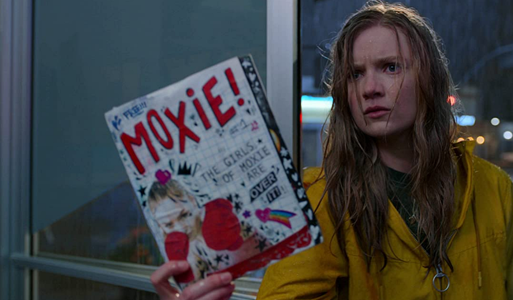 Screenshot of Vivian standing in the rain holding up her Moxie zine.