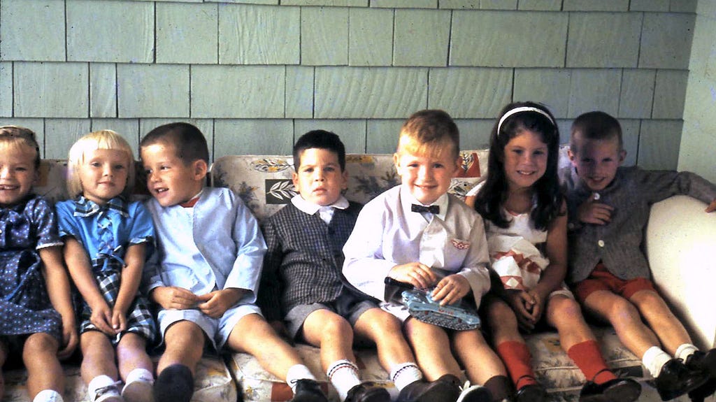 Seven smiling 5 and 6-year-old boys and girls, dressed for a party, squeezed side-by-side on a couch