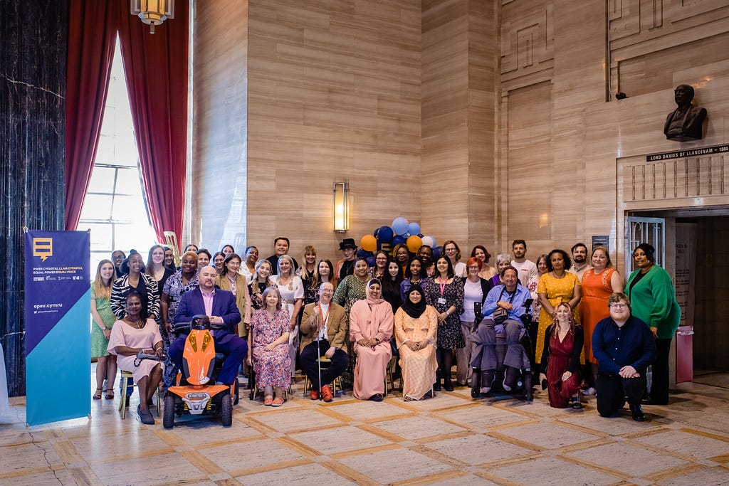 A large group of people pose and (mostly) smile for a picture in a grand looking room