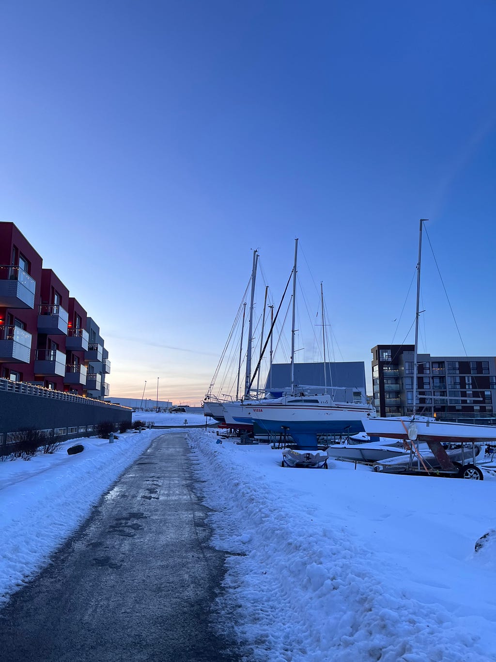 Image of boats parked in a snowy port, buildings in the background