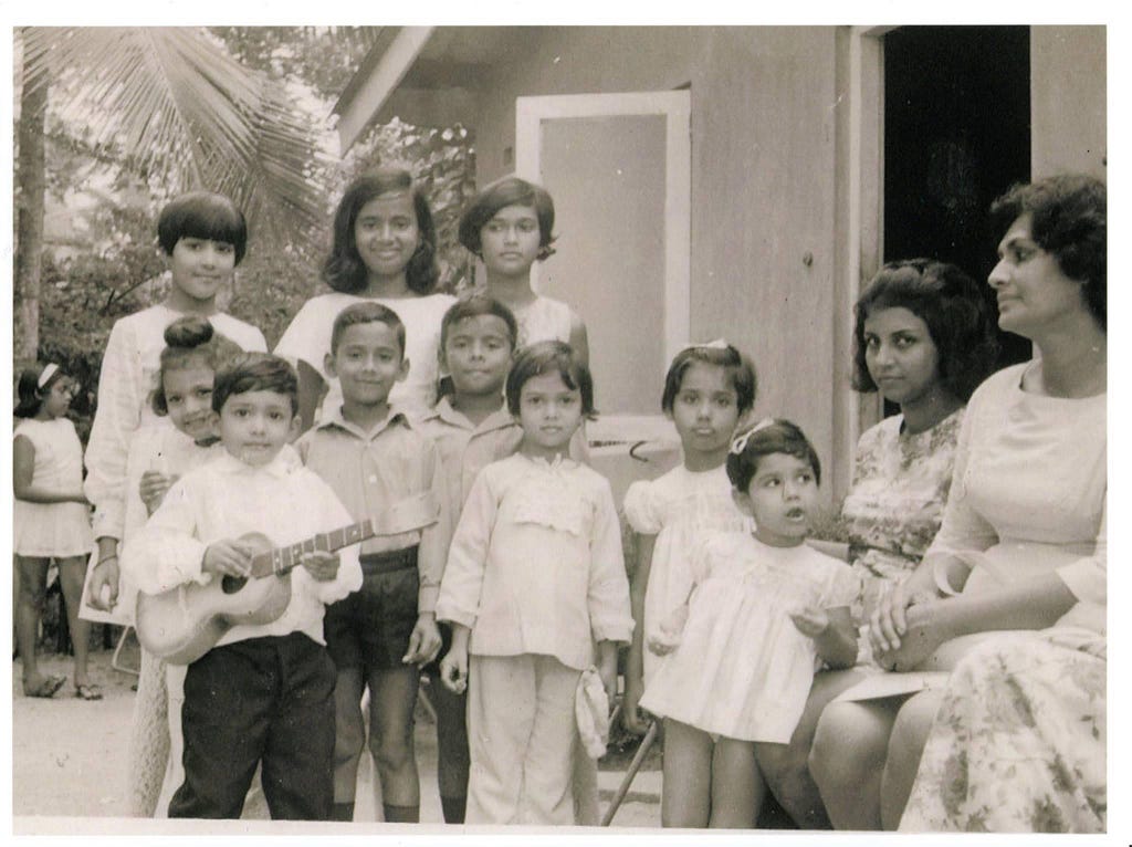 A black and white photograph of a group of people posing for the camera at a party. The author is wearing black pants and a white shirt, holding a toy guitar.