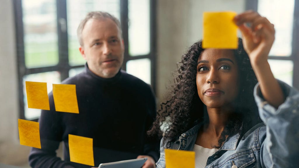 A man and a women sticking post-its on a wall.