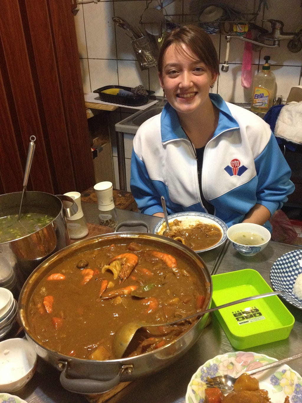 Megan smiles sitting at a table with a big pot of curry.