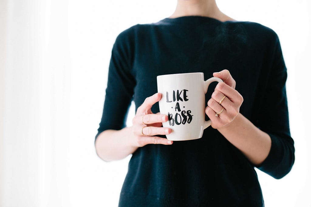 A woman holding a coffee mug having text ‘like a boss’