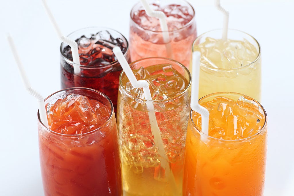 An assortment of fruit cocktails with white bendy straws in them.