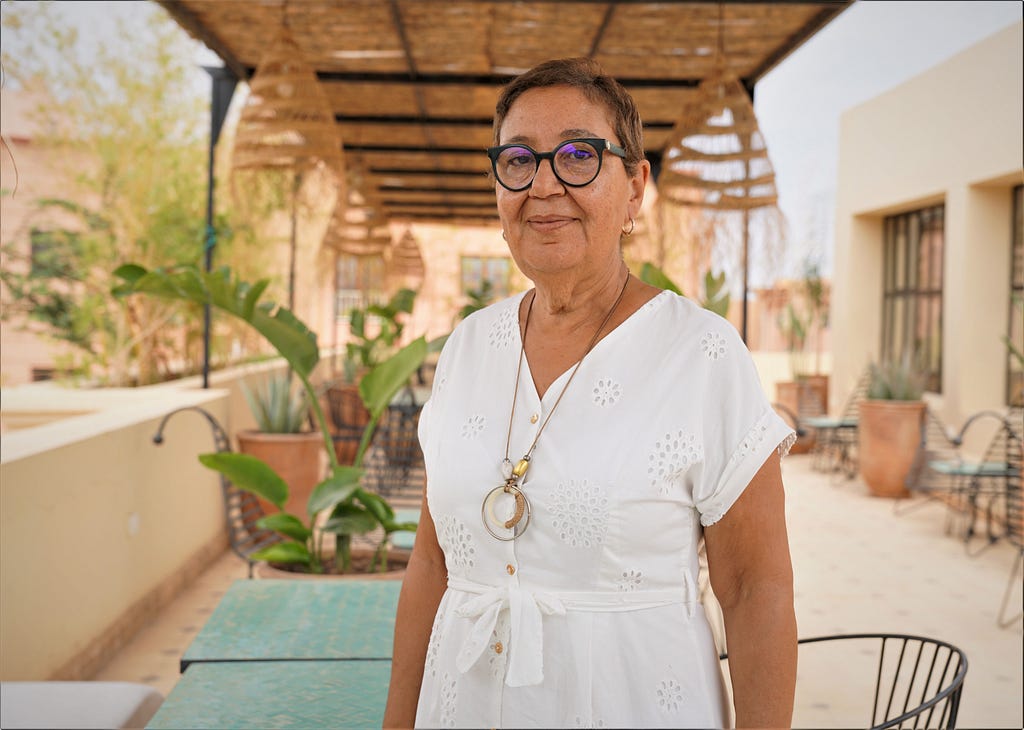 A Moroccan woman smiles and proudly stands in a rooftop restaurant looking at the camera.