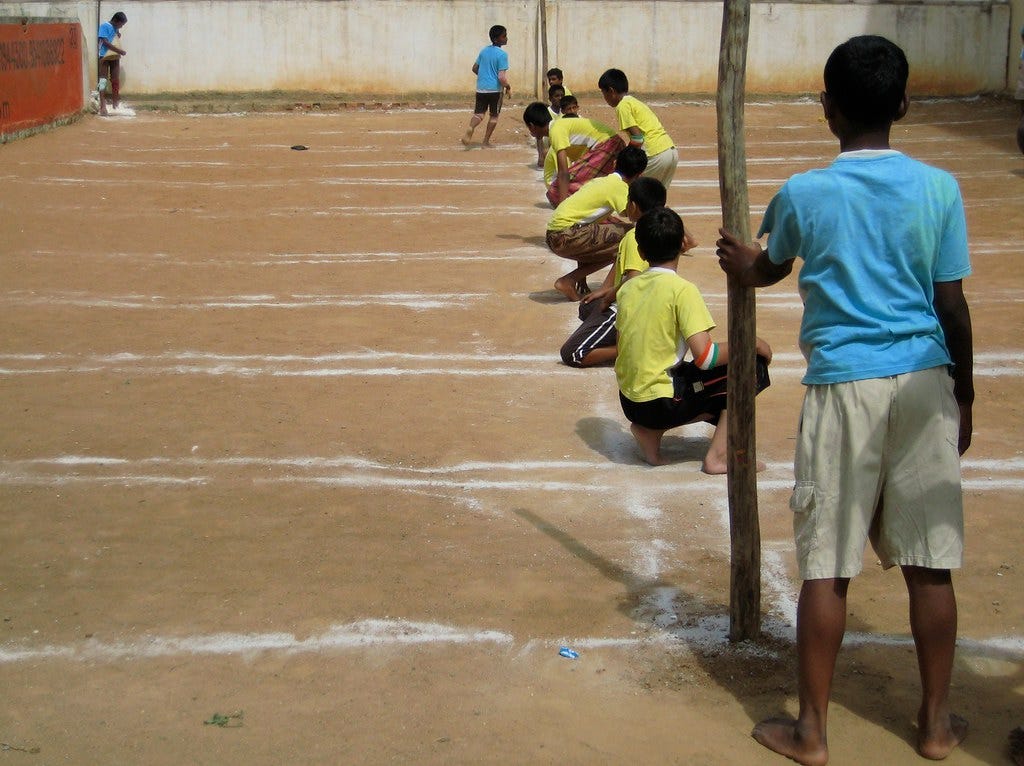 The yellow team of schoolboys is sitting to chase, while the two players from the blue team of defenders are standing on either side of the two poles.