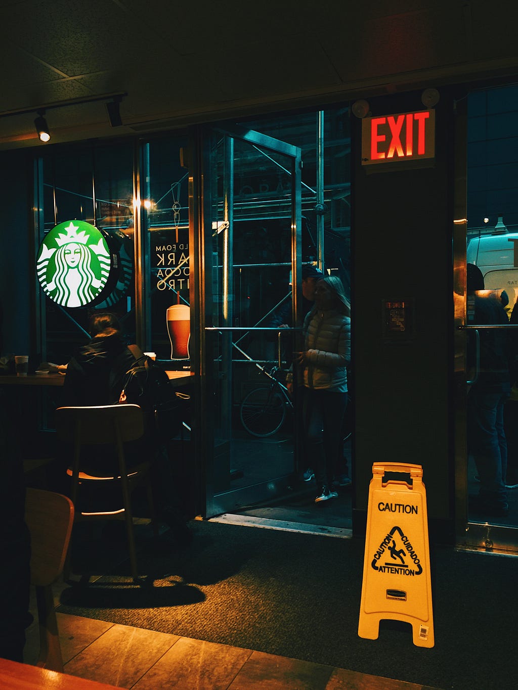 The dark interior of a Starbucks coffee shop with a yellow “Caution” floor sign.