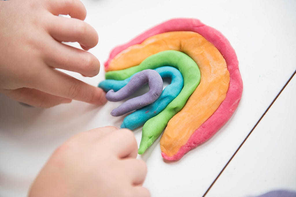 Two hands making a rainbow out of playdough