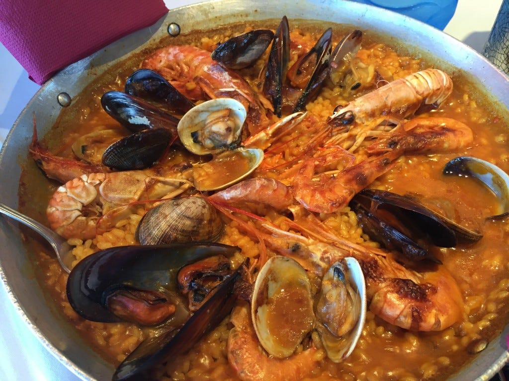 A close up of a very large pan of paella, complete with clams, muscles and whole prawns on the top and in their shells