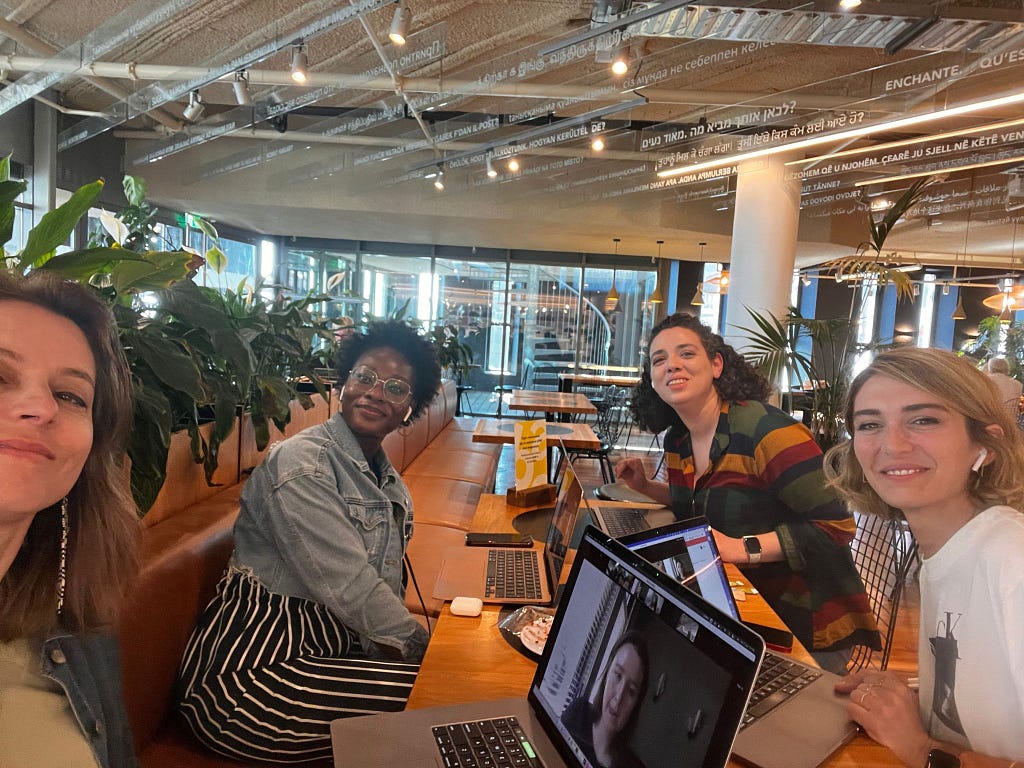 Four women sitting in the library with their laptops studying and happy to see each other after 2 weeks working together remotely