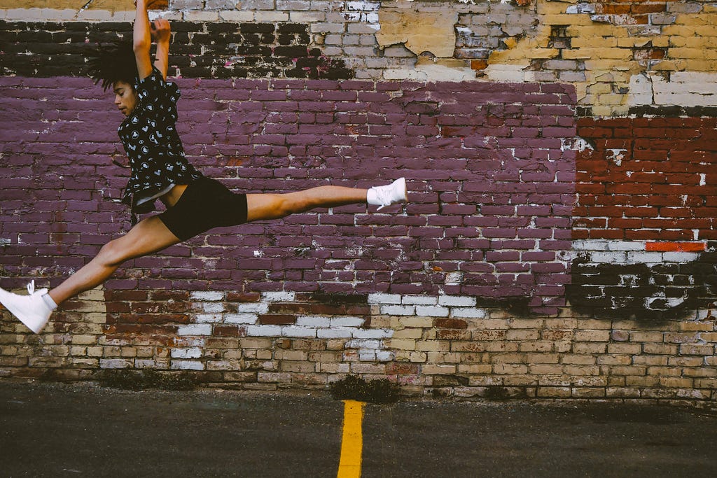 black woman leaping in front of a brick wall