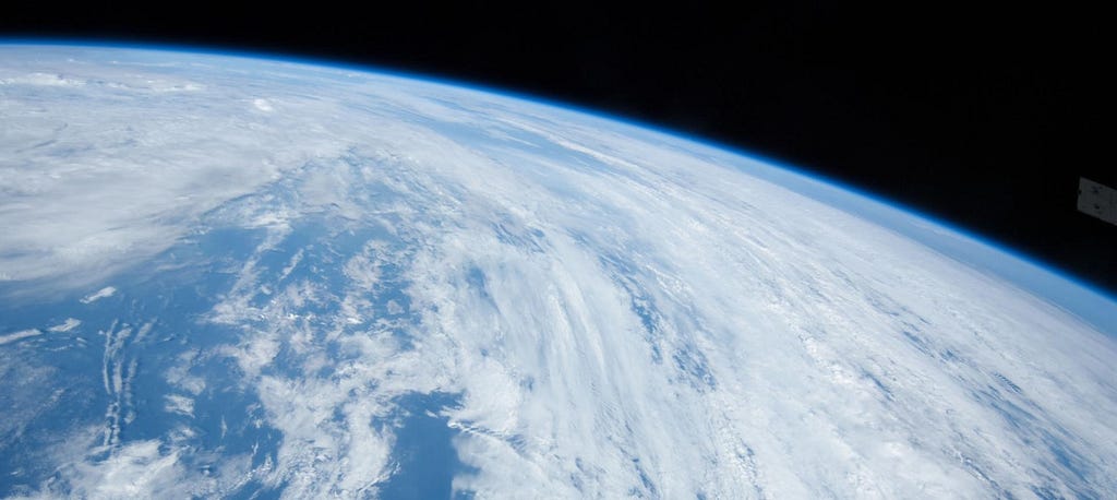 A photograph of Earth taken from the International Space Station. It shows a vast expanse of blue sea and cloud cover.