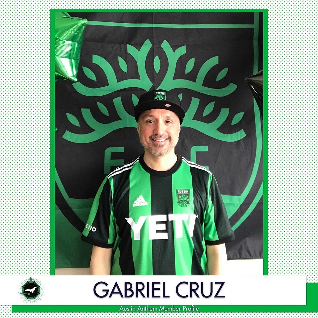 An image of Gabriel Cruz, who is wearing an Austin FC hat and jersey, standing in front of the Austin FC flag