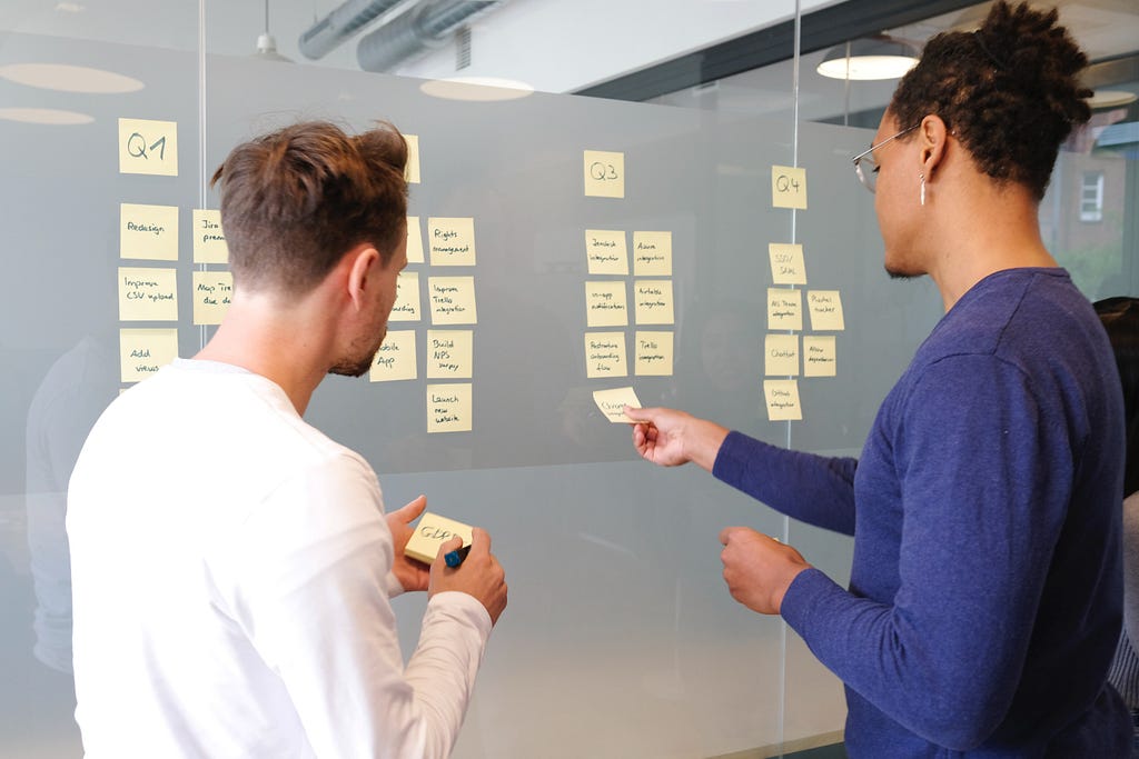 Two people placing a series of post-it notes on a glass divider.