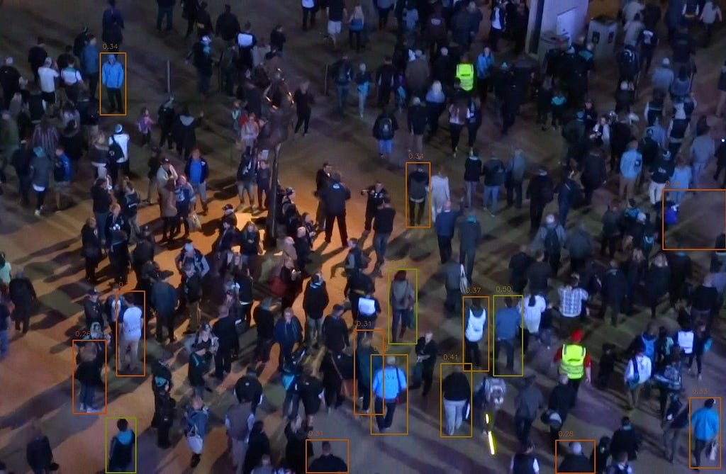 Une image d’une foule de nuit, en extérieur. Certaines personnes sont entourées d’un cadre, d’autres non.