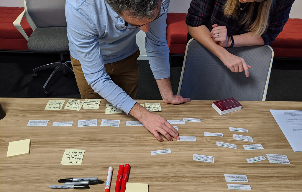 Photo of two people arranging sticky notes and pieces of paper with quotes on them into a linear sequence.