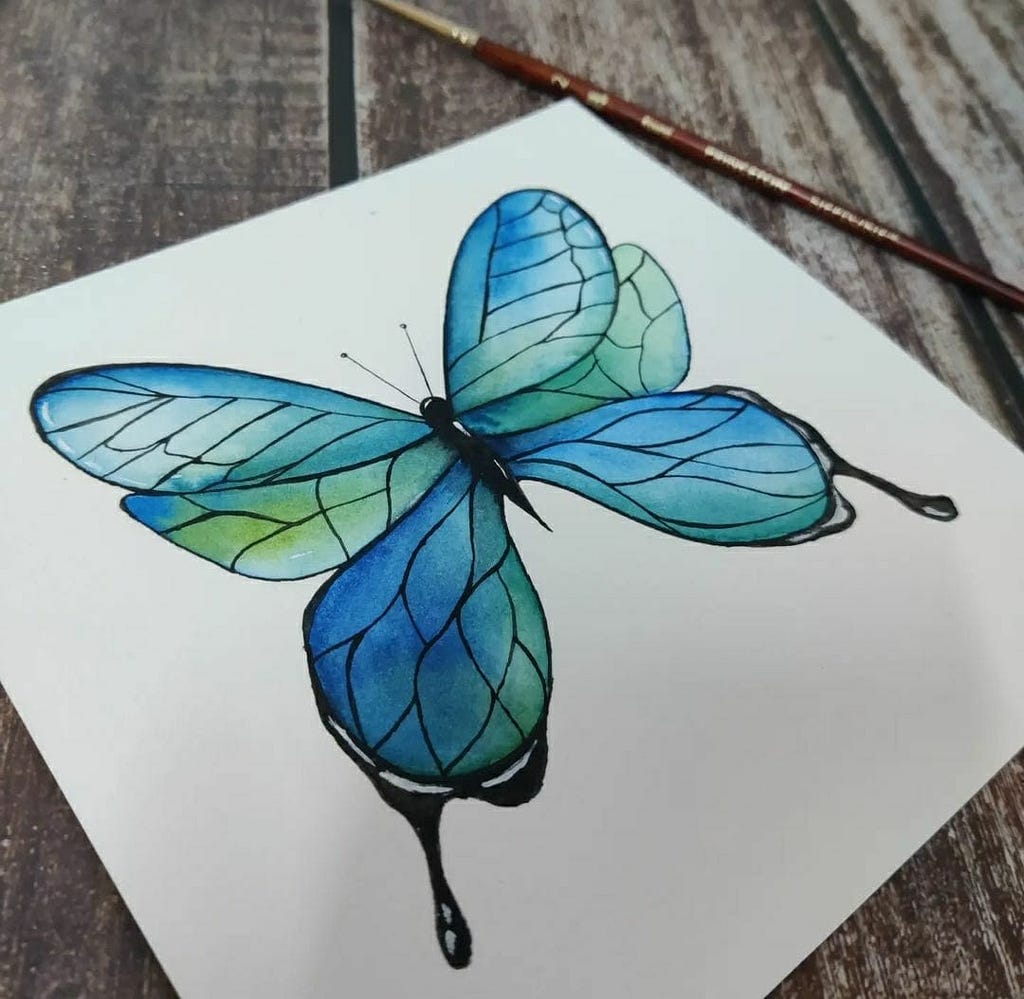 A watercolor butterfly — blue and green in color on a paper.