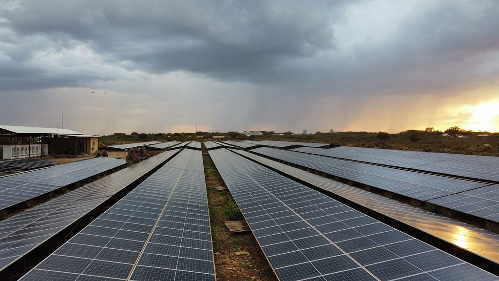 Rows of solar panels in a solar plant with stormy clouds and rain in the distance.