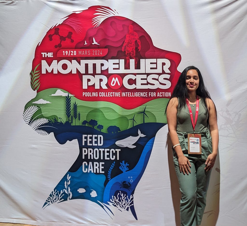 Ankitha standing at the MGD24 event in front of a sign that says ‘The Montpellier Process’