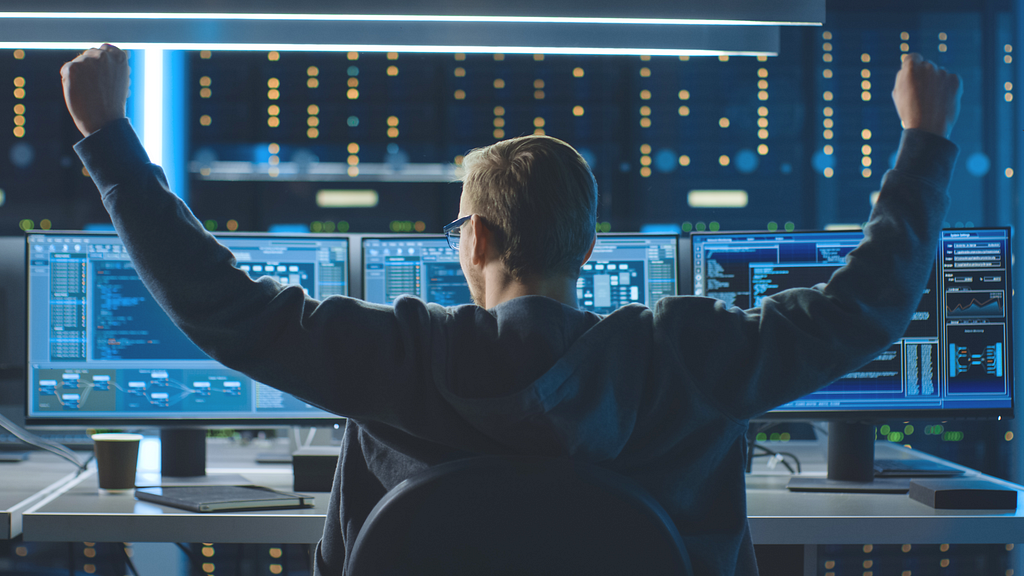 Happy cyber security or IT security specialist sitting in front of the computer monitor and raising his hands because choosing the best cyber security training