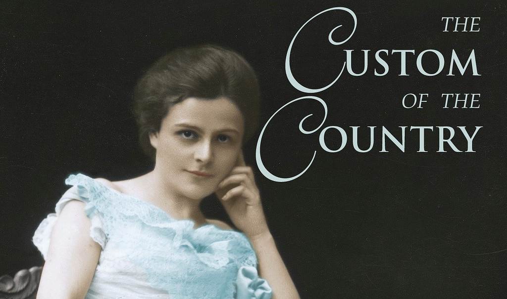 A woman with light skin and brown hair sits staring at the camera against a black background. She wears a light blue early-20th-century dress, and the words “The Custom of the Country” appear to her right.