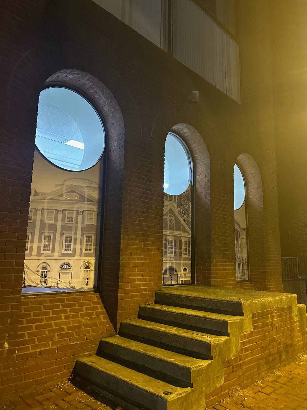 Three brick-arched windows are backlight at night, each displaying sepia toned antique photographs in poster form of Georgian style buildings.