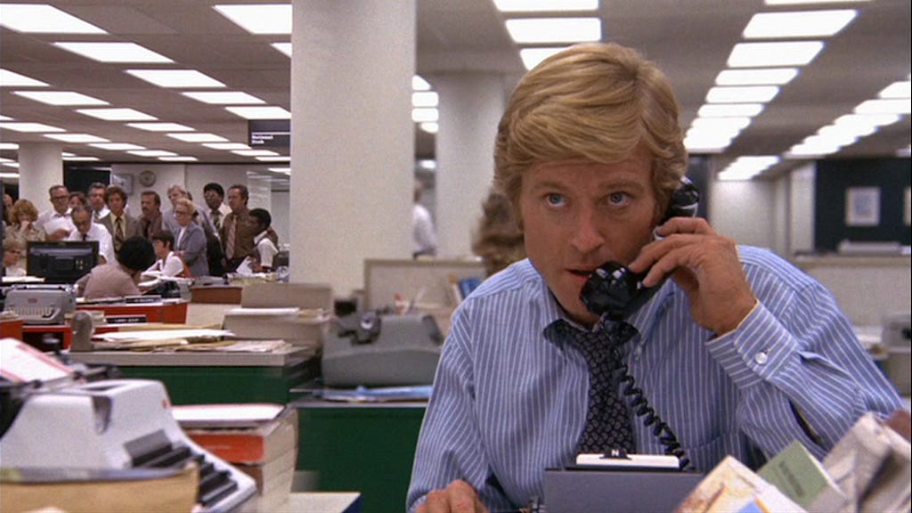 Still from the movie All the President’s Men. Robert Redford is on the telephone in a newsroom.