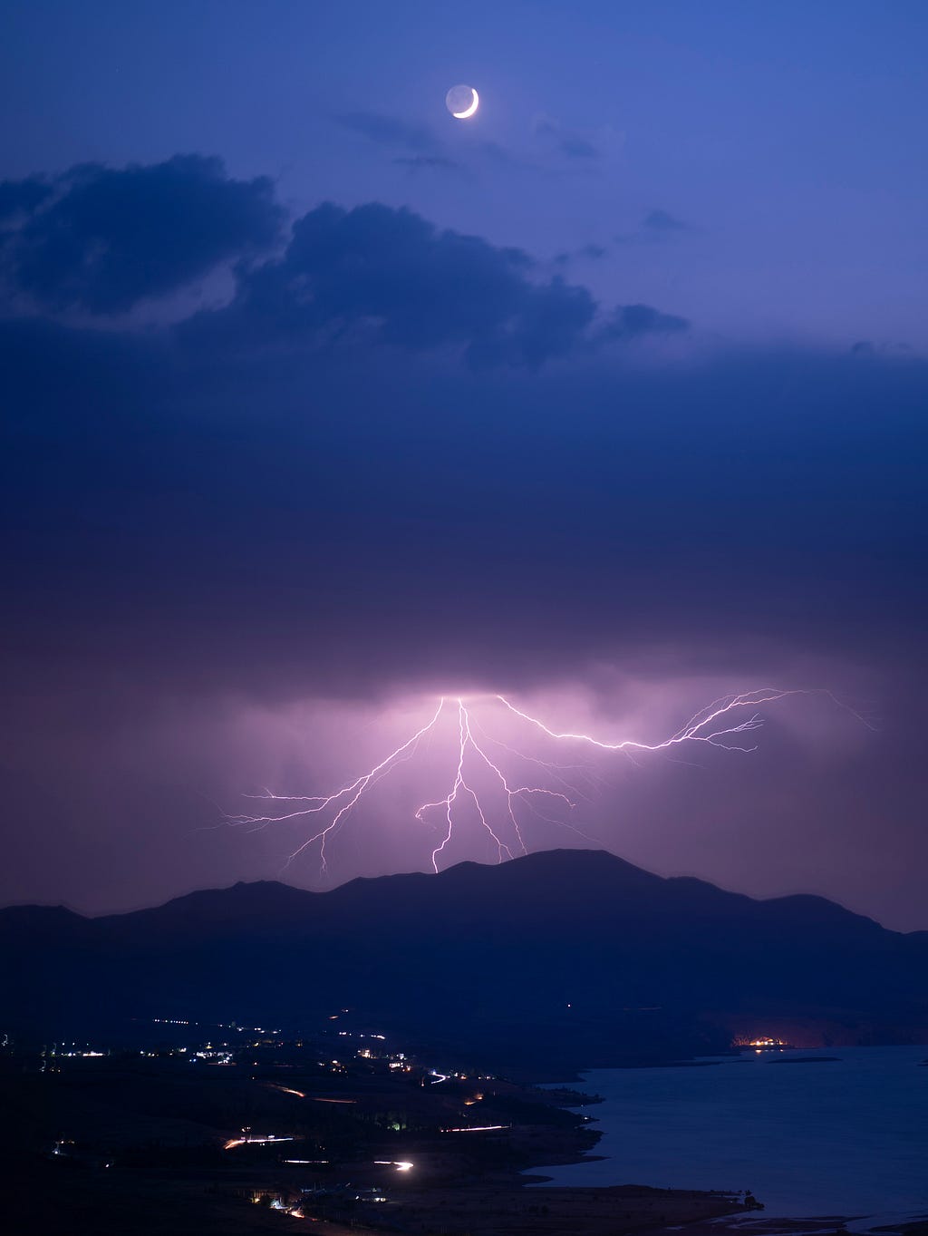 A dramatic scene with a crescent moon and a flash of lightning over a landscape.