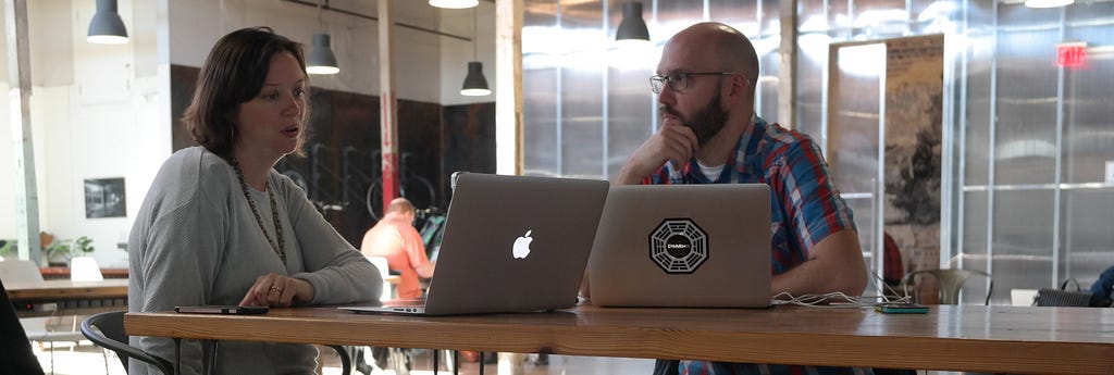 Woman and man in conversation at an office with their laptops open