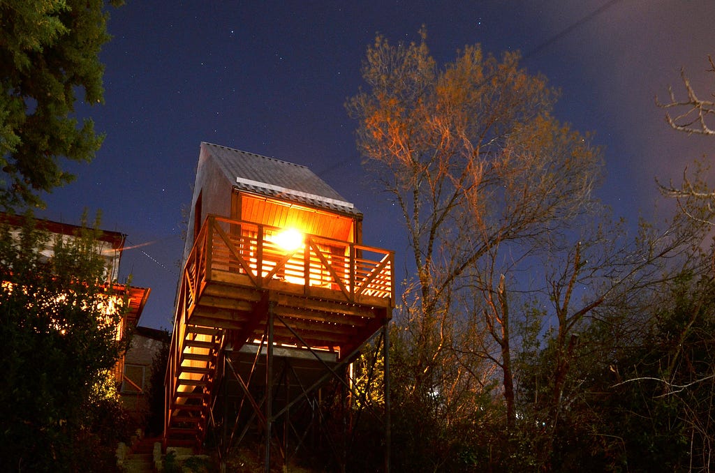 elevated wood and metal cabin lit up at night