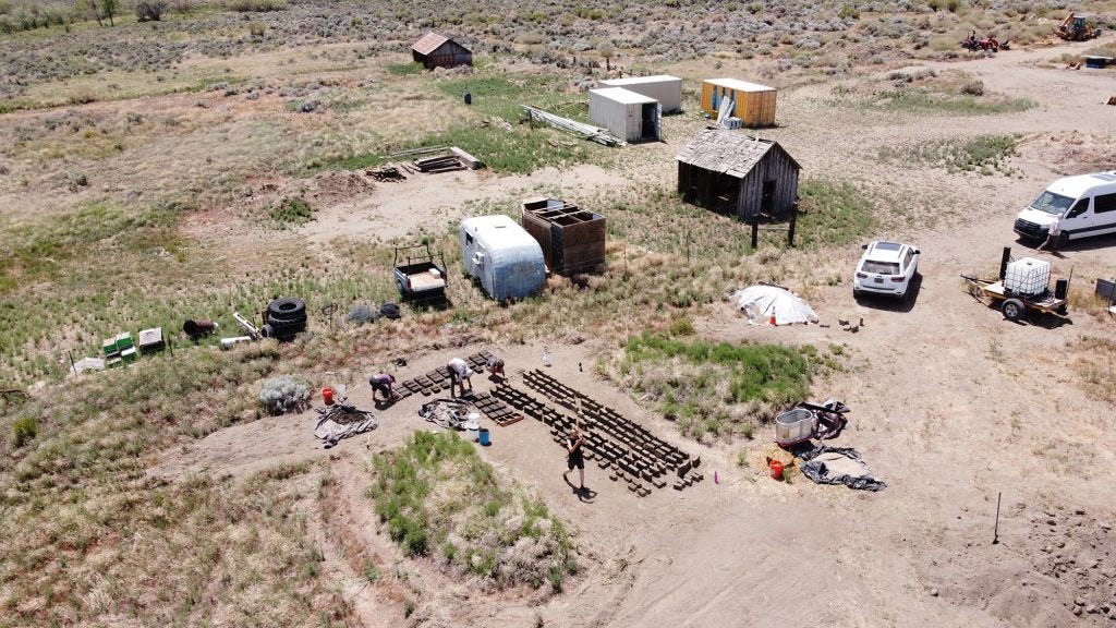 Aerial photo of the SEED site showing the cob bricks drying in the sun surrounded by people working, trailers, cars, and old buildings.