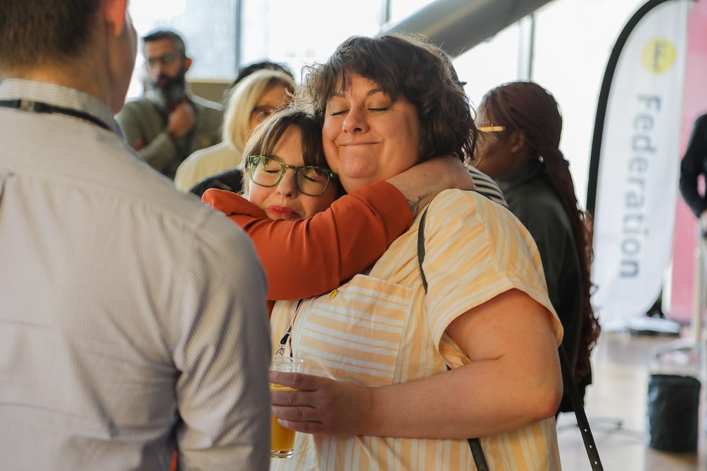 Two women with their eyes closed hug each other tightly whilst smiling.